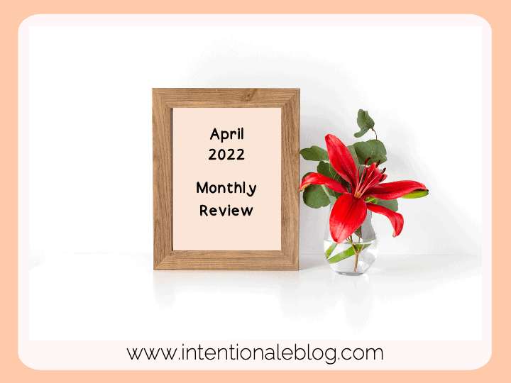 Image of a wooden frame beside a glass vase with red flowers and green leaves. Frame has text; April 2022 Monthly Review