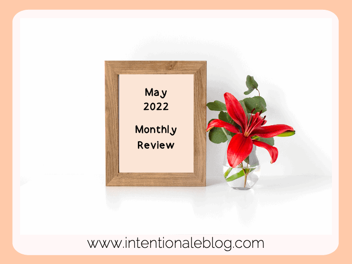 image of a brown frame with text: may 2022 monthly review, there's a glass vase with red flower beside the frame